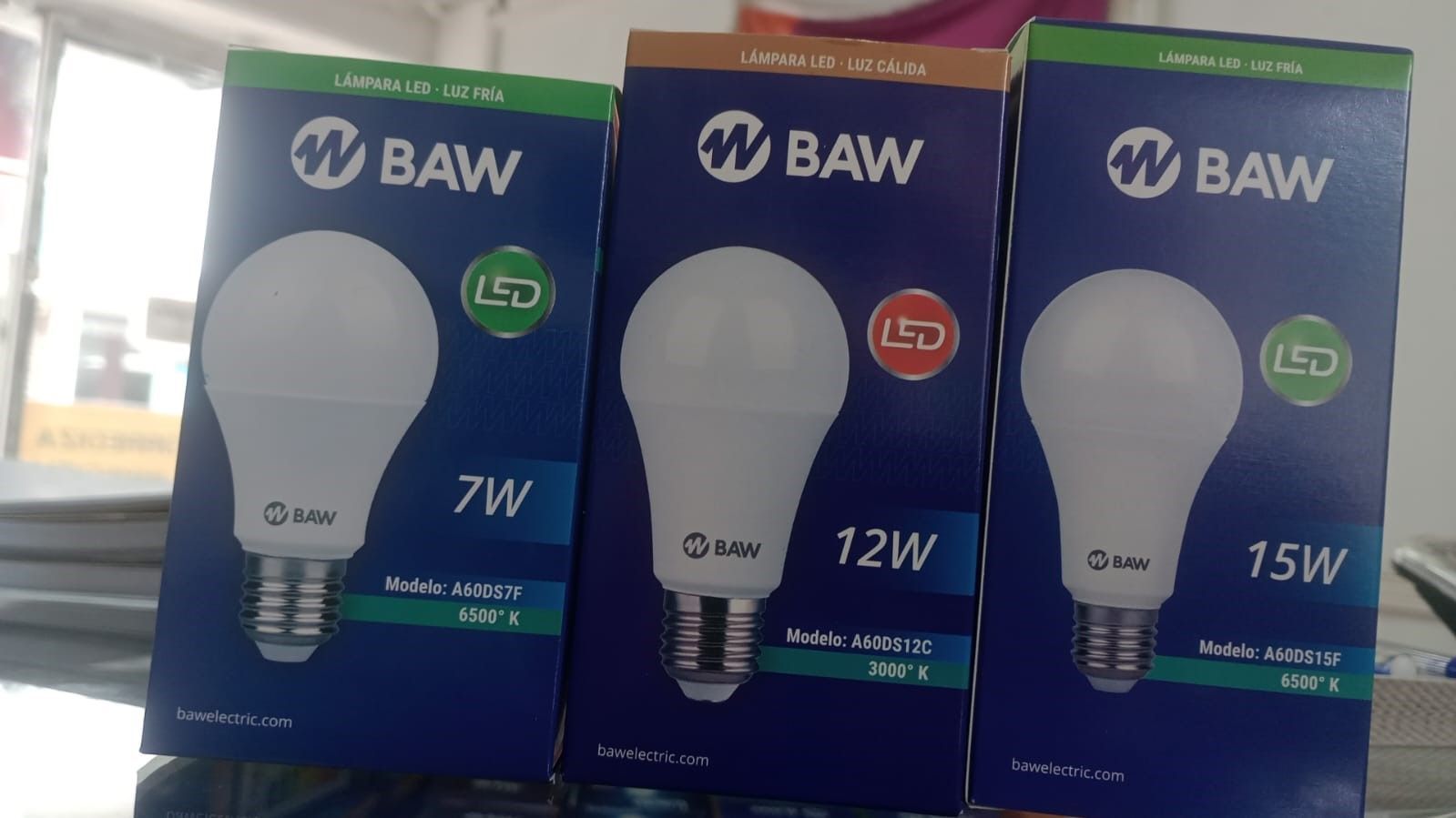 Tres cajas de bombillas LED BAW, etiquetadas como 7W, 12W y 15W, con fondo azul y bombillas blancas.