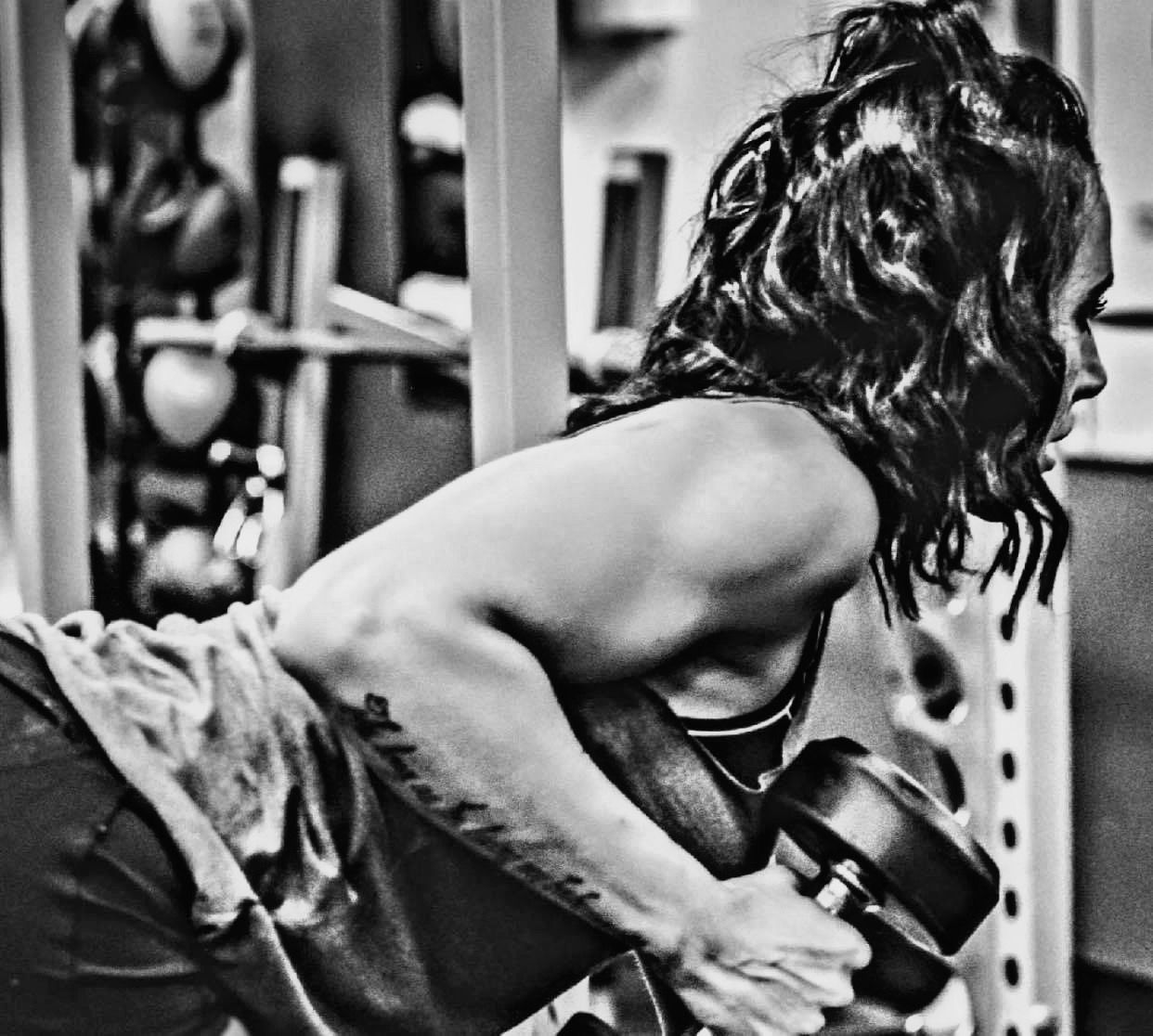 A woman with a tattoo on her arm is lifting a dumbbell in a gym.
