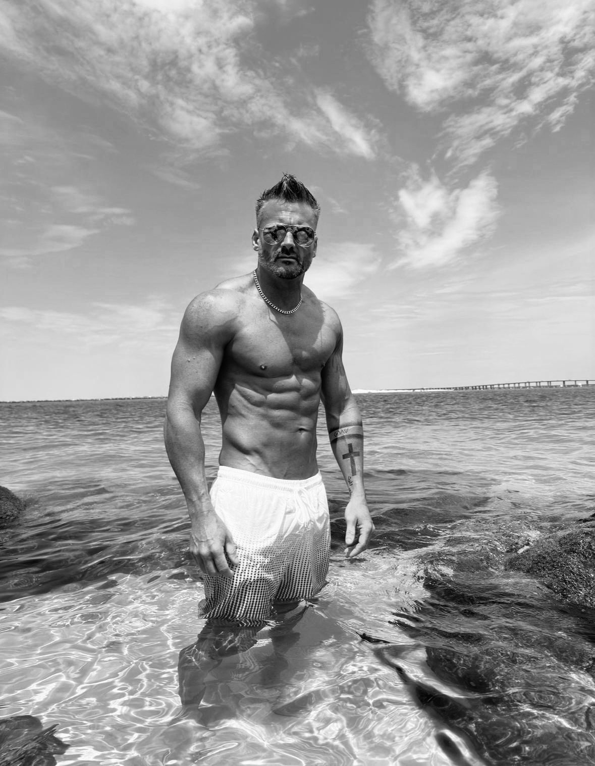 A shirtless man is standing in the water on the beach.