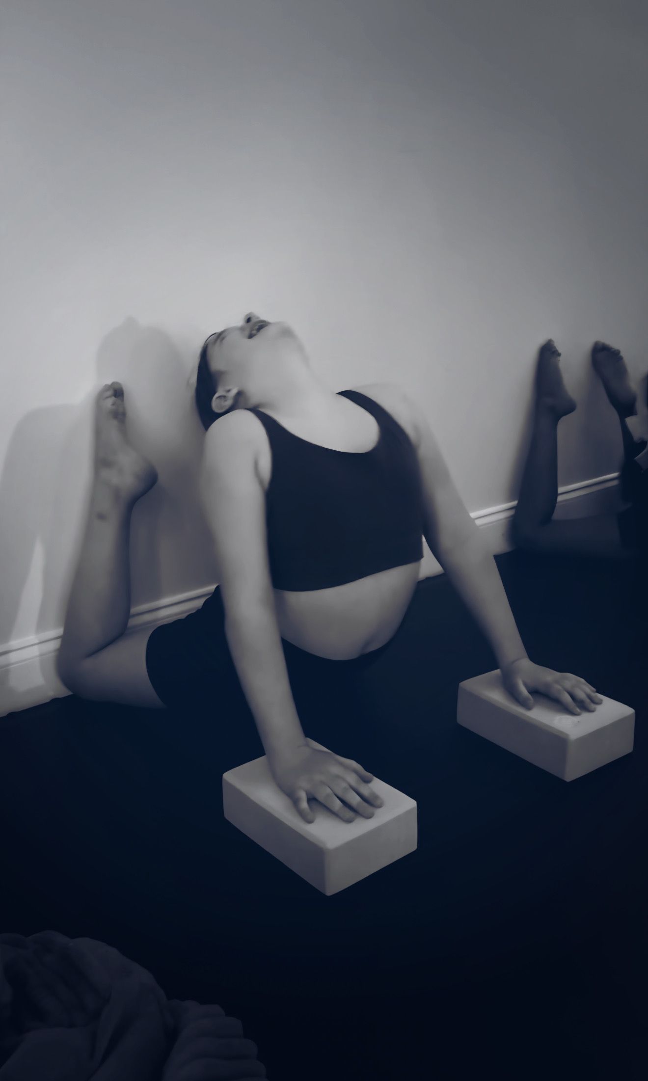 Person in yoga pose against a wall, using blocks for support. Black and white photo.