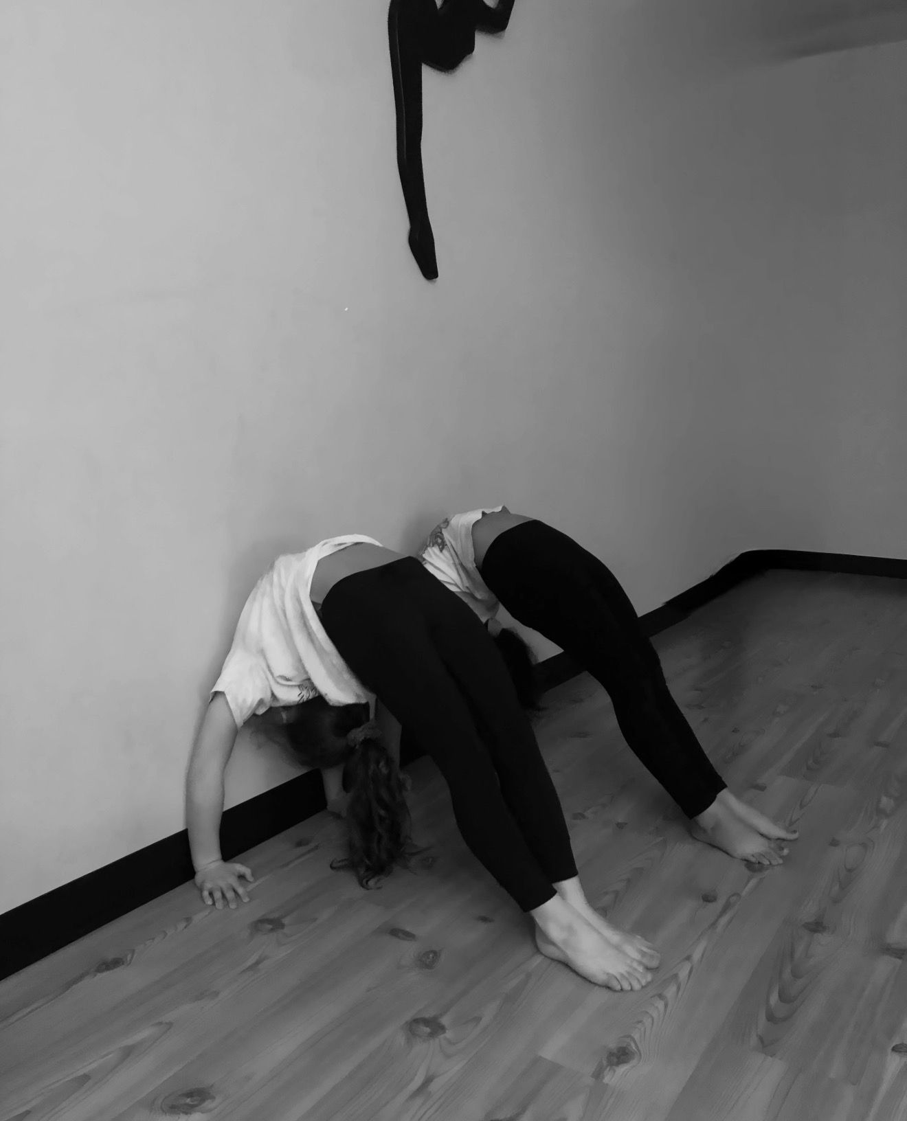 Two people arched backward, hands on floor, legs extended, against a wall in a room.