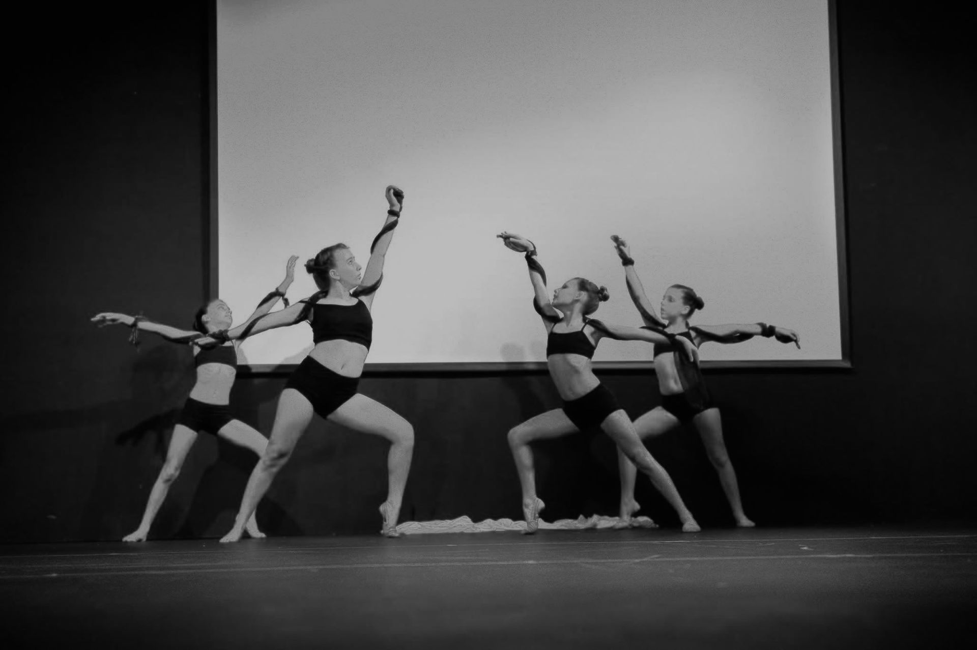 Dancers in black tops and shorts performing on stage with arms raised.