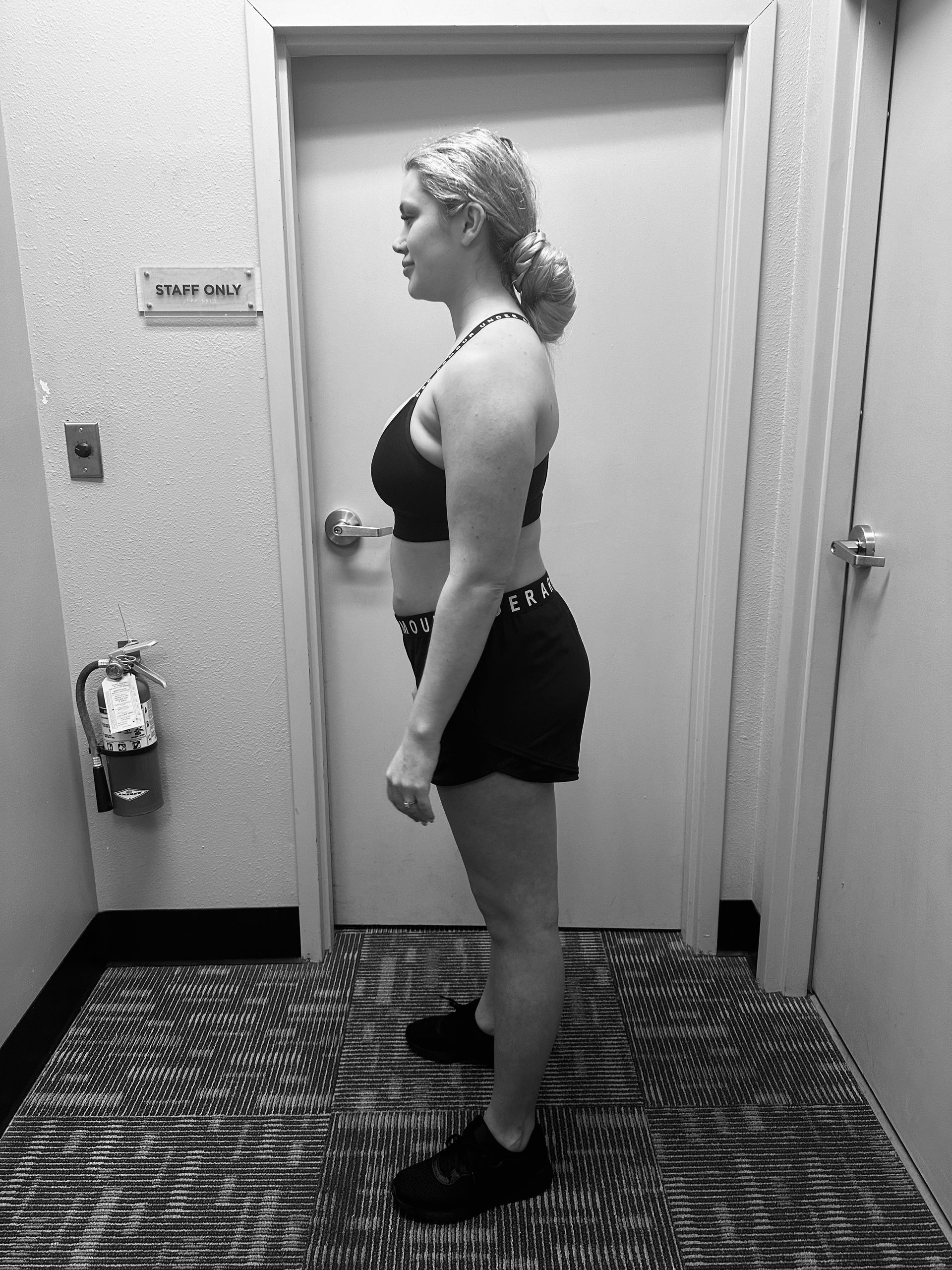 A woman is standing in a hallway in front of a door.