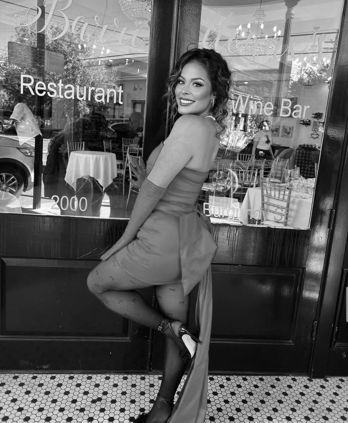 A woman in a dress is standing in front of a restaurant window.