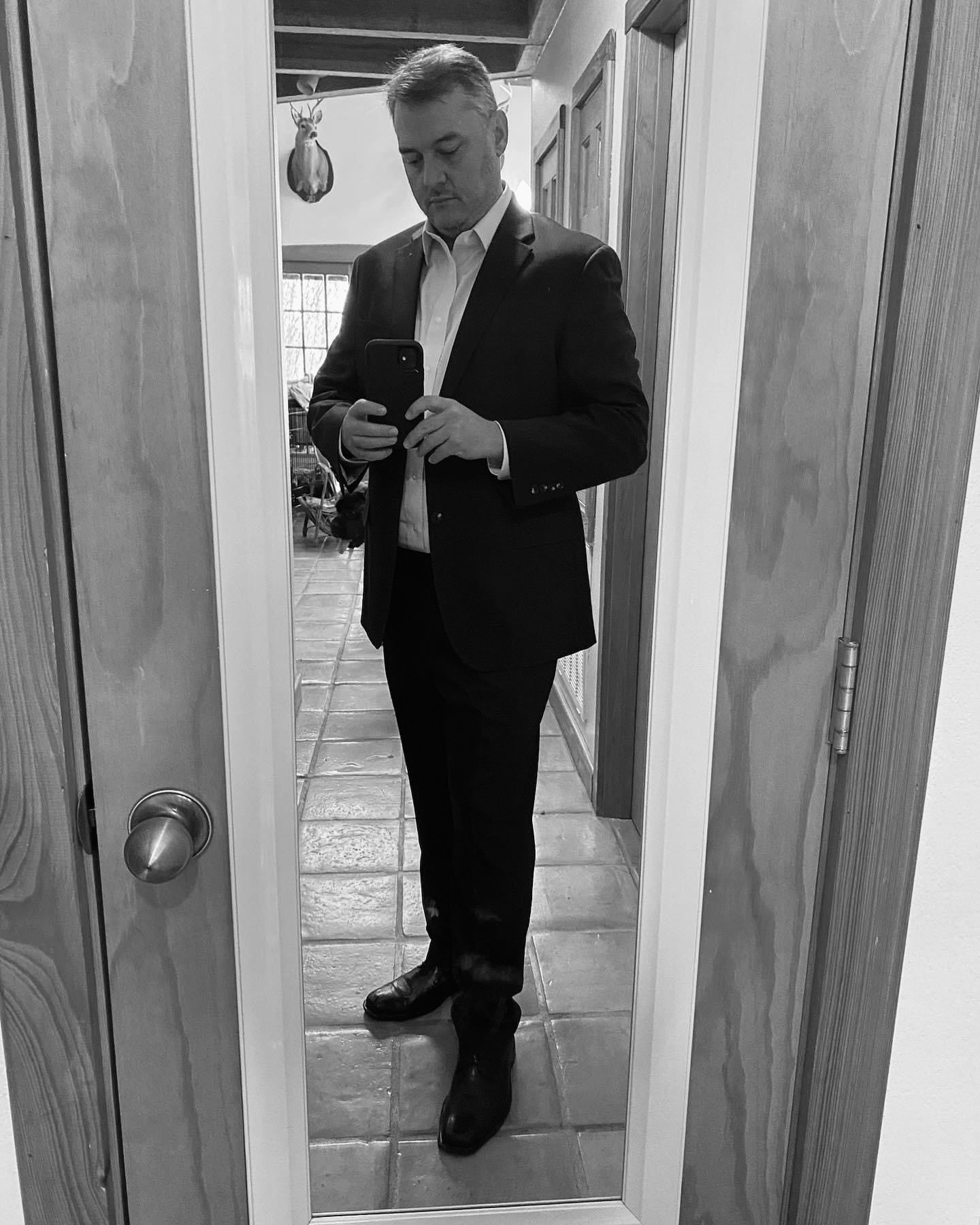 A man in a suit is standing in front of a mirror.