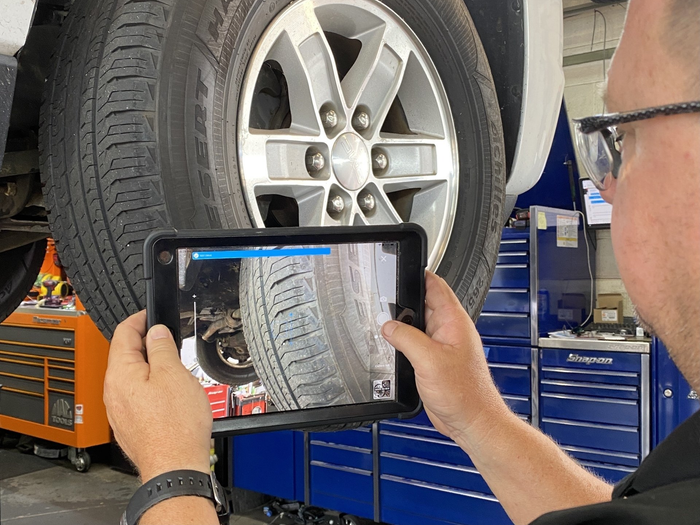 Mechanic photographing a car tire and wheel with a tablet in an auto repair shop