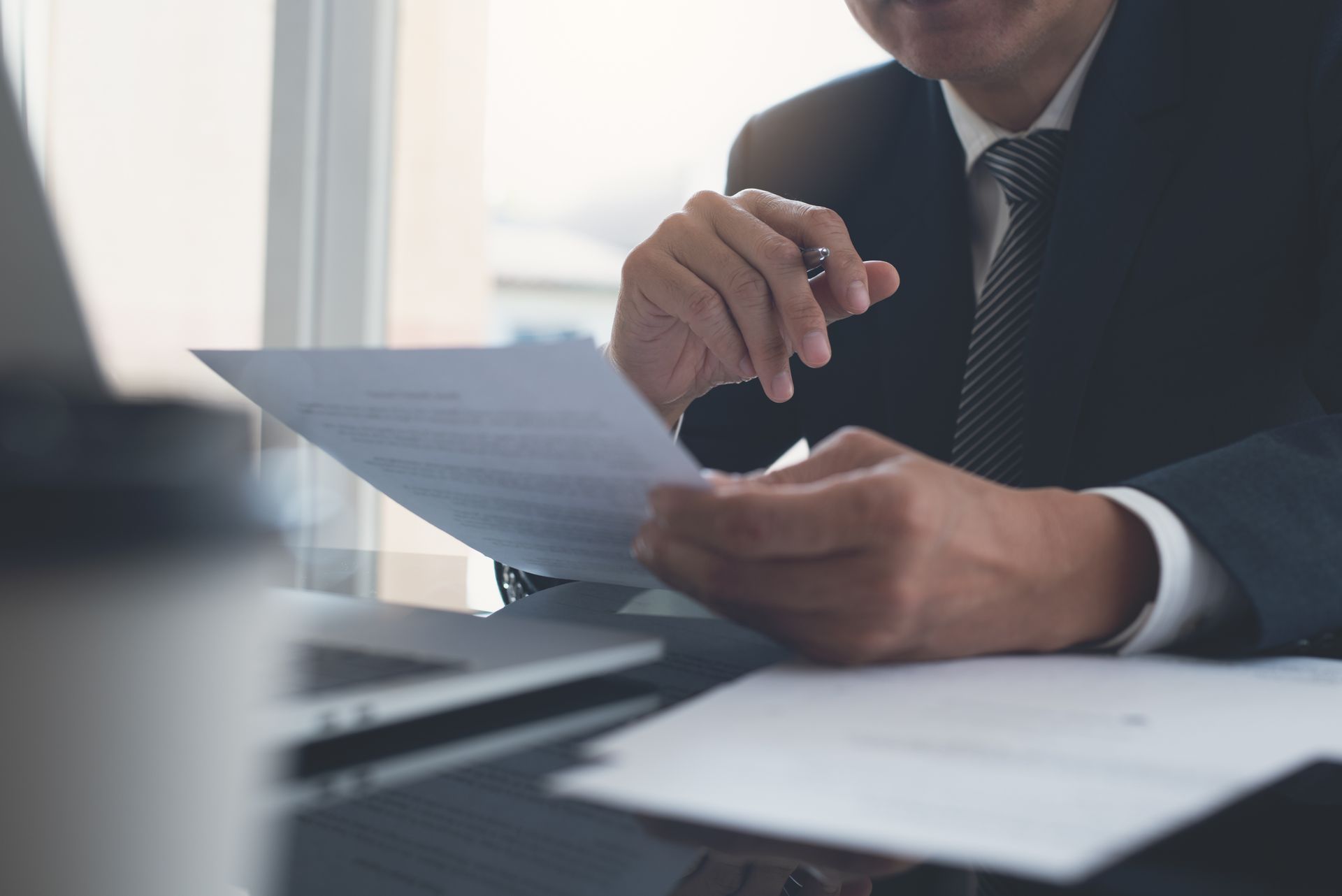 A man in a suit and tie is sitting at a desk looking at a piece of paper.