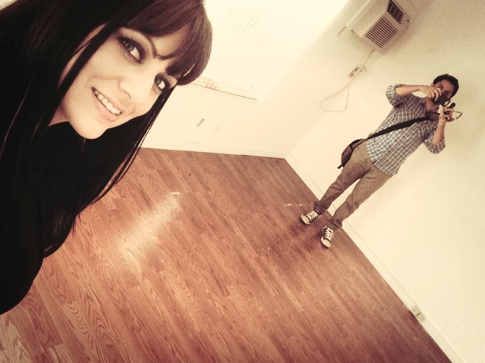 Woman smiling, taking a selfie. Man taking a photo with a camera in a room with wood floors.