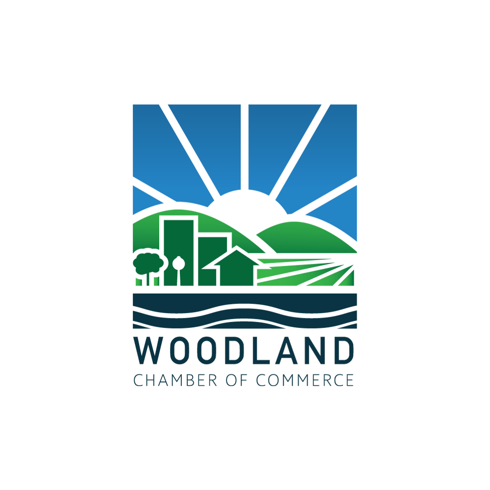 Woodland Chamber of Commerce logo: Blue sky, sun, green hills, buildings, water, text.
