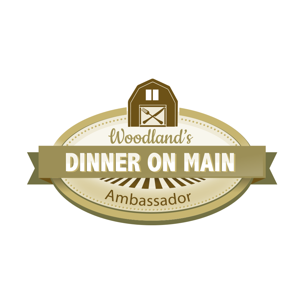 Woodland's Dinner on Main Ambassador logo: oval with text, barn icon, gold and brown.