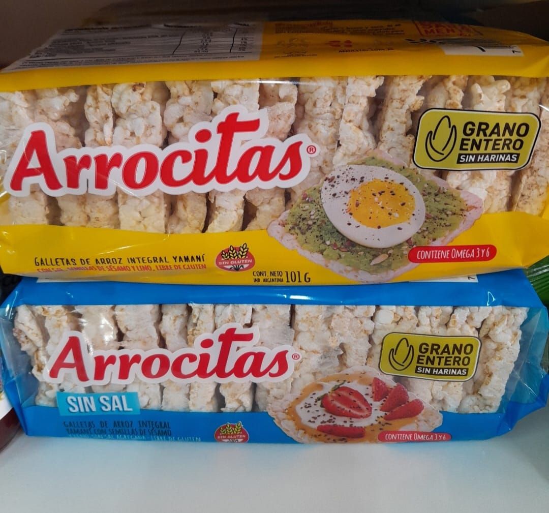 Dos paquetes de tortas de arroz “Arrocitas”, una amarilla, otra azul; de grano entero y un snack.