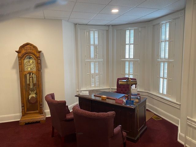 A room with a desk , chairs and a grandfather clock.