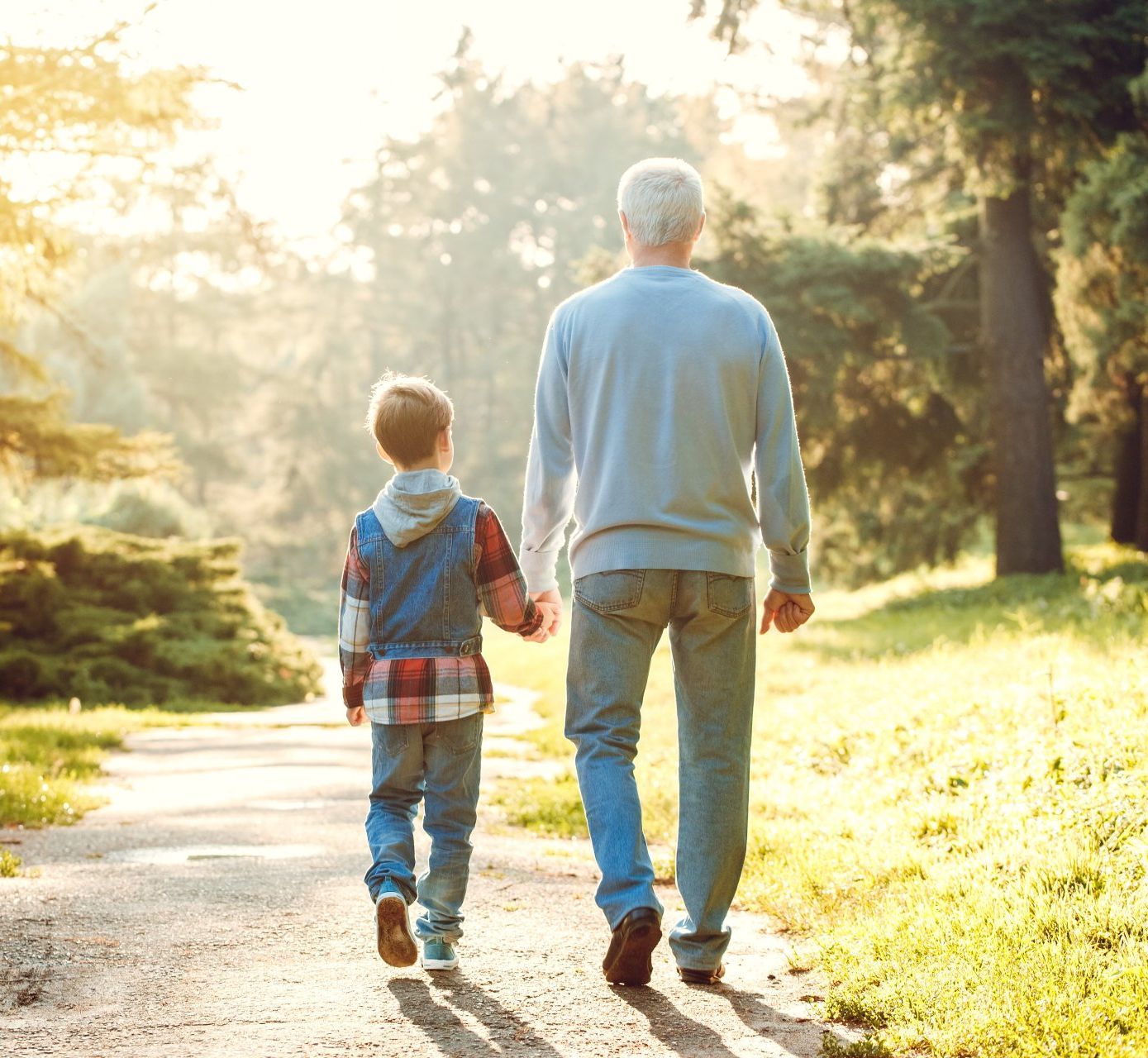 An elderly man and a young boy are walking down a path holding hands.