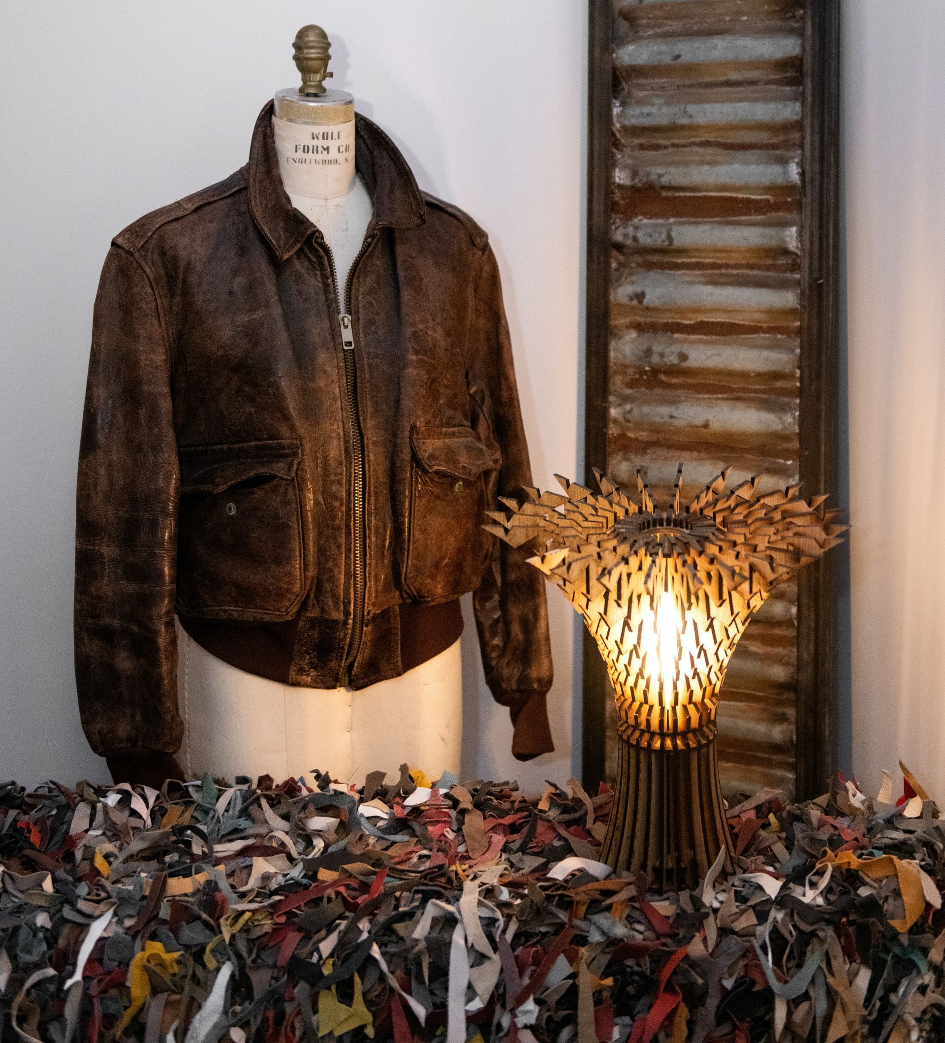 A brown leather jacket is on a mannequin next to a lamp