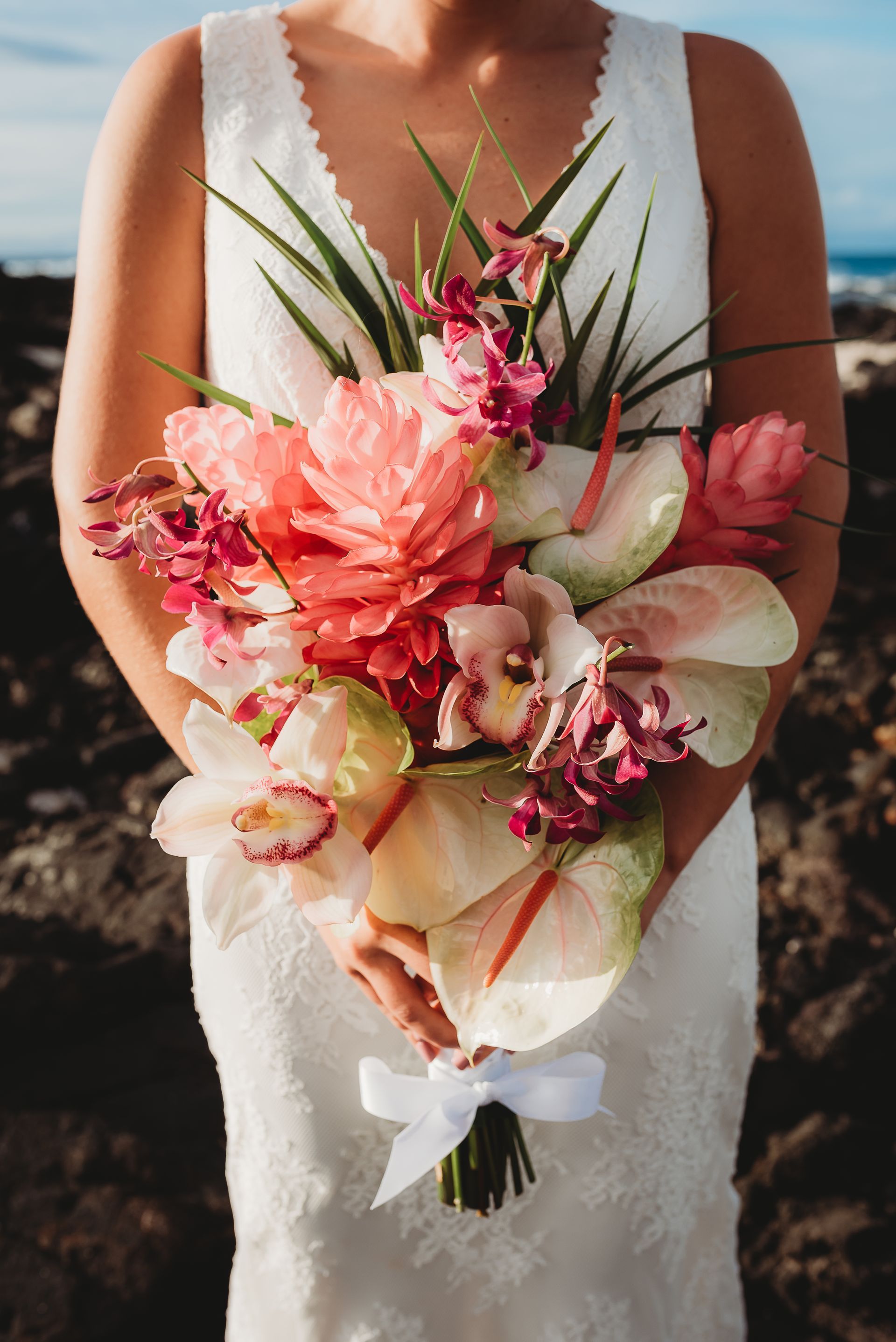 Bride holding a pink and white tropical bouquet in a white dress on a beach