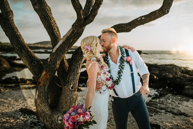 Newlyweds kiss as guests toss flower petals at beach wedding. Simple Kona Beach Weddings.