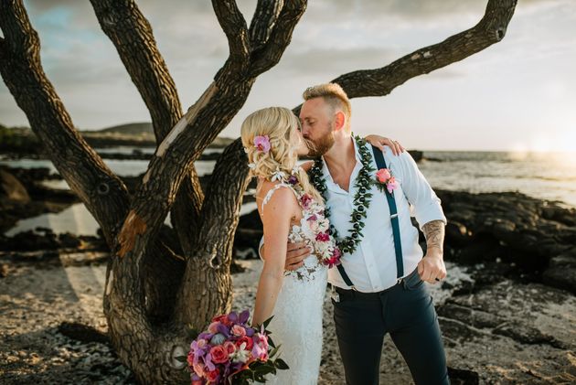 Newlyweds kiss as guests toss flower petals at beach wedding. Simple Kona Beach Weddings.