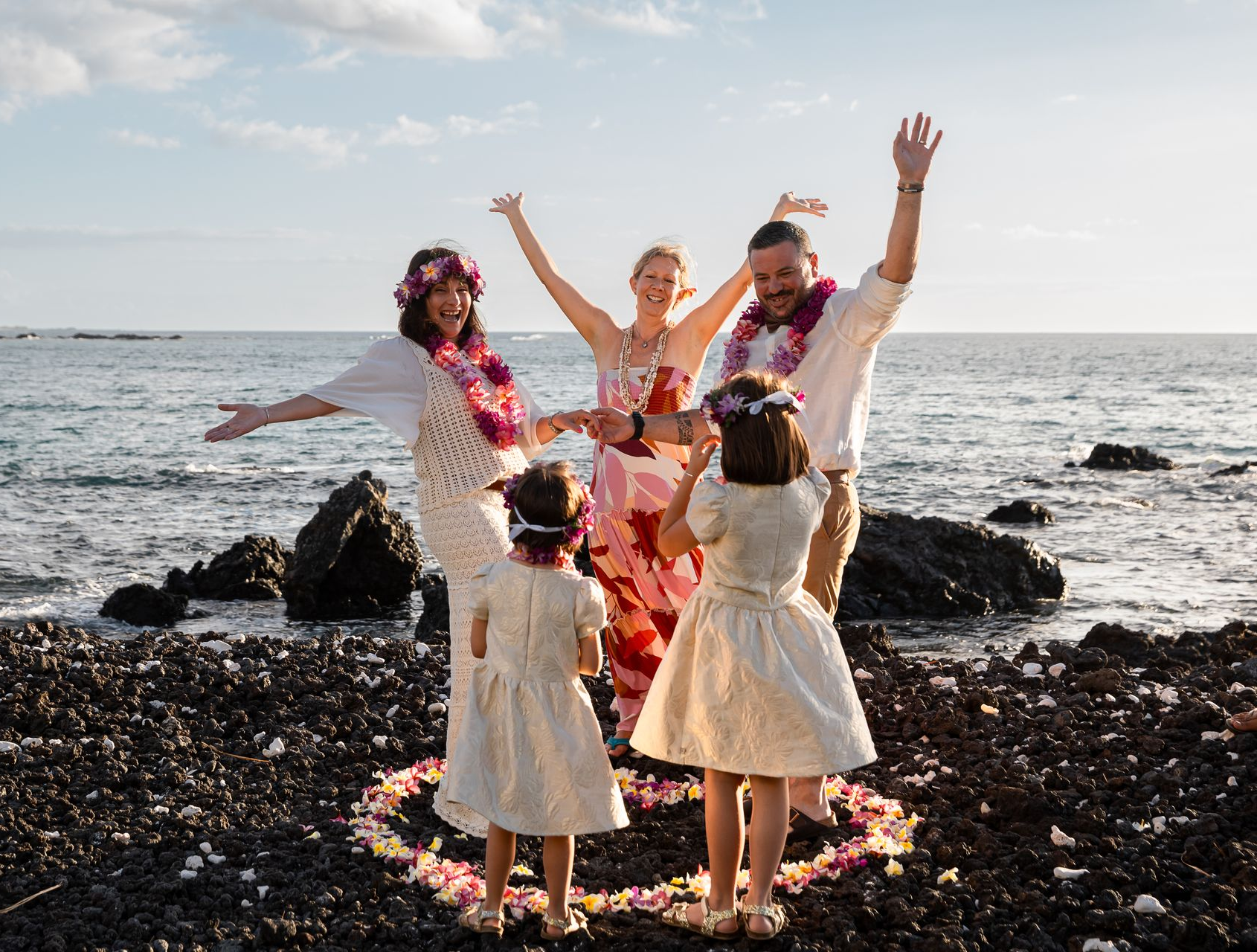 Couple holding hands at outdoor wedding ceremony on rocks near water.