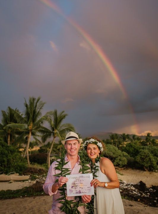 Couple holding hands at outdoor wedding ceremony on rocks near water.