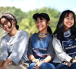 Three happy young women are sitting next to each other and smiling.