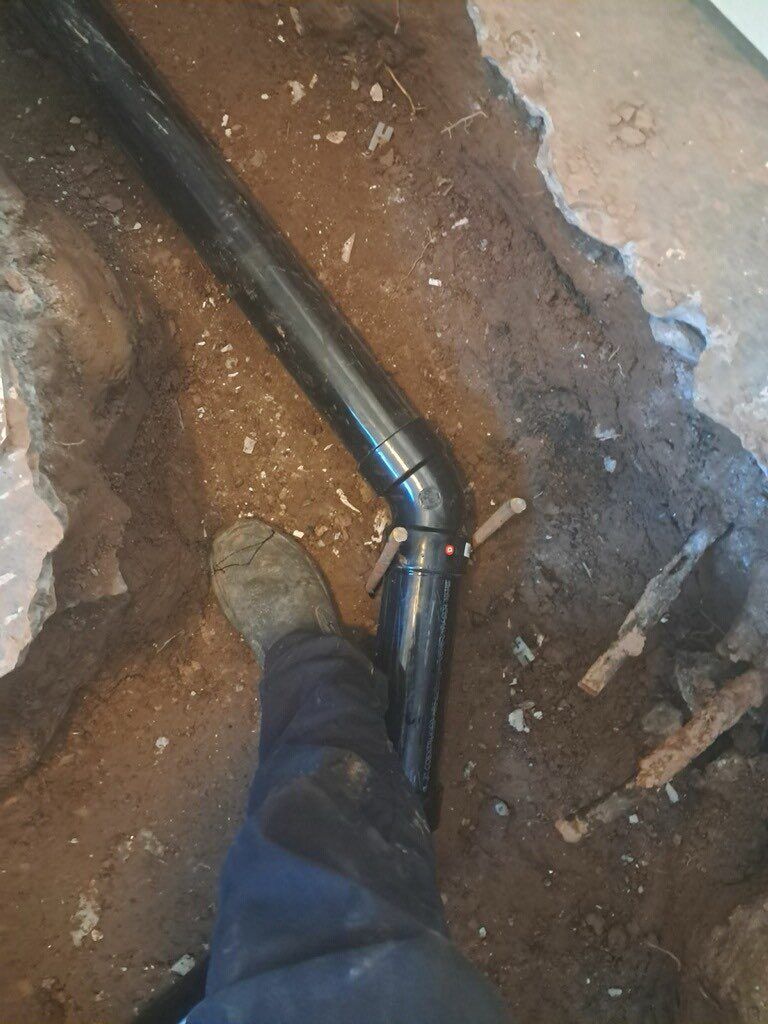 A person is standing next to a pipe in the dirt.