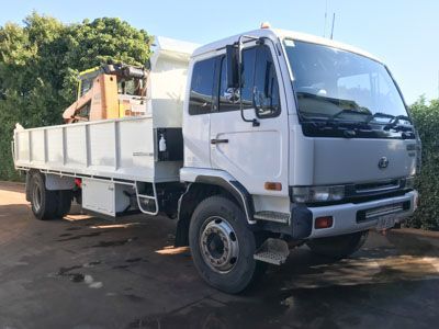 A white dump truck with a crane attached to the back is parked on a dirt road.