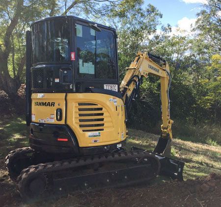 A small yellow excavator is parked in the middle of a field.