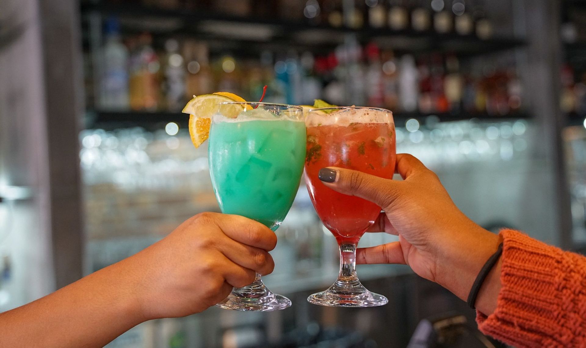 two people are toasting with cocktails at a bar .