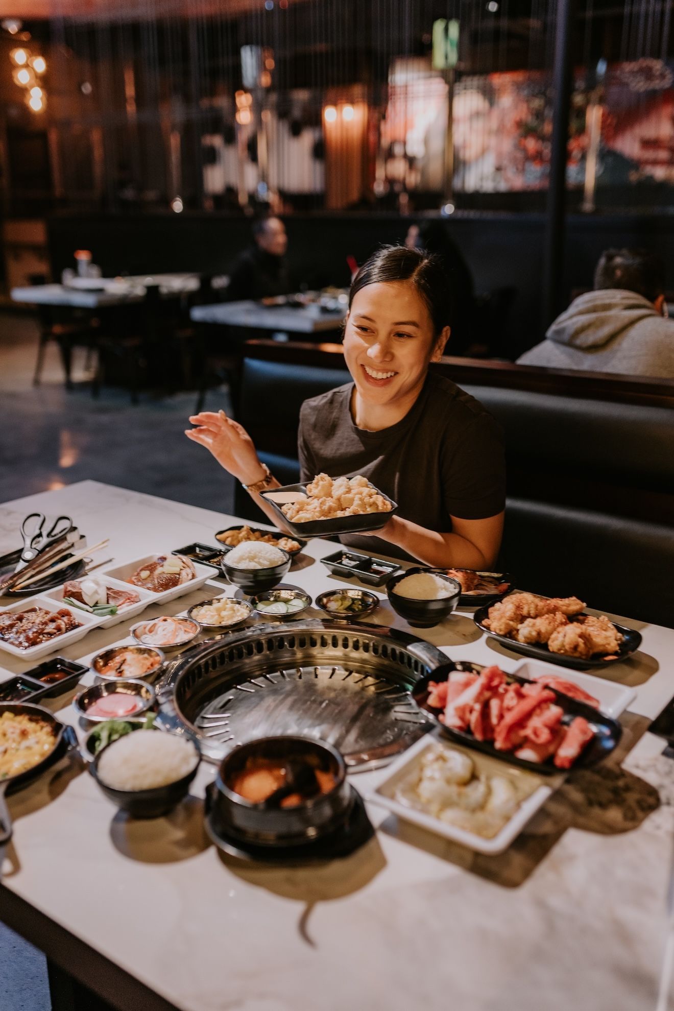a woman is sitting at a table in a restaurant eating Korean BBQ food .