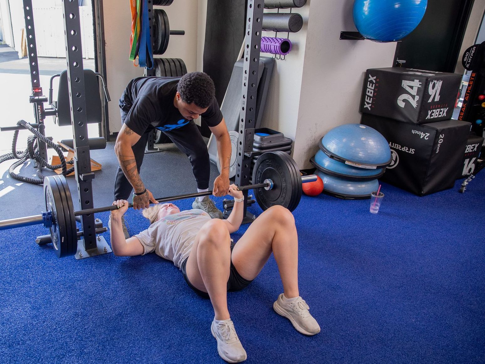 A man is helping a woman lift a barbell in a gym.