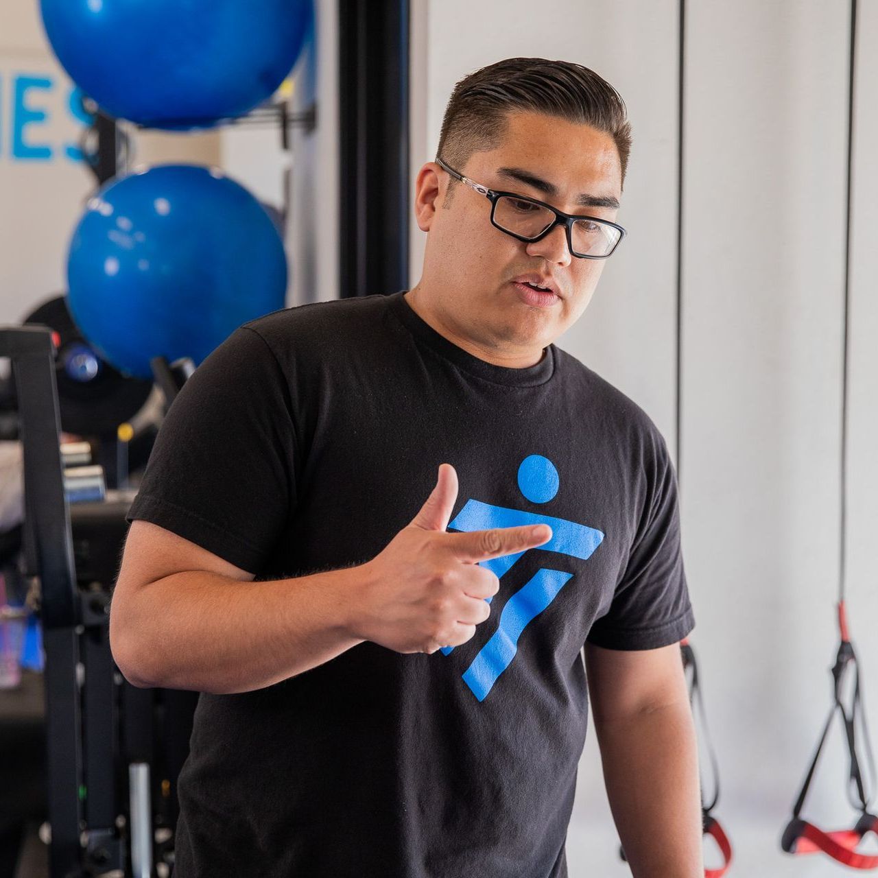 A man wearing glasses is giving a thumbs up in a gym