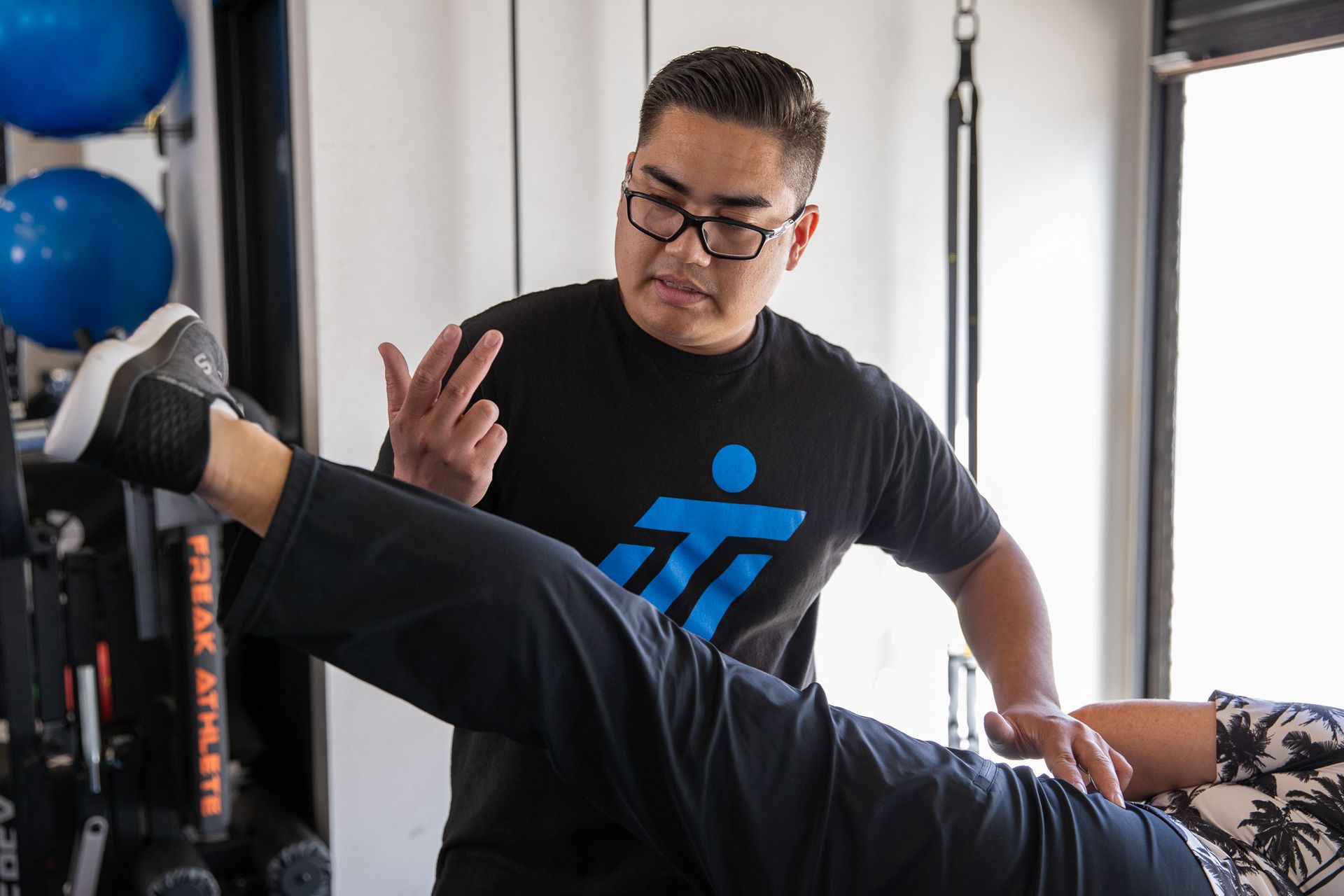 A man is helping a woman stretch her legs in a gym.