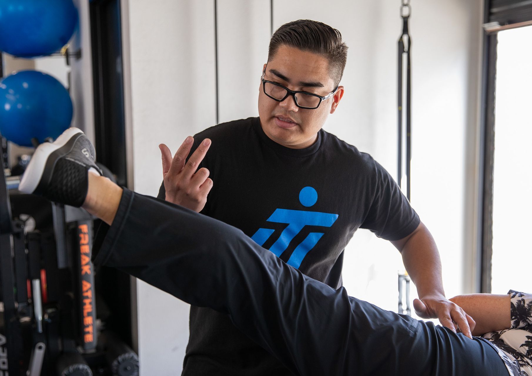 A man is stretching a woman 's leg in a gym.