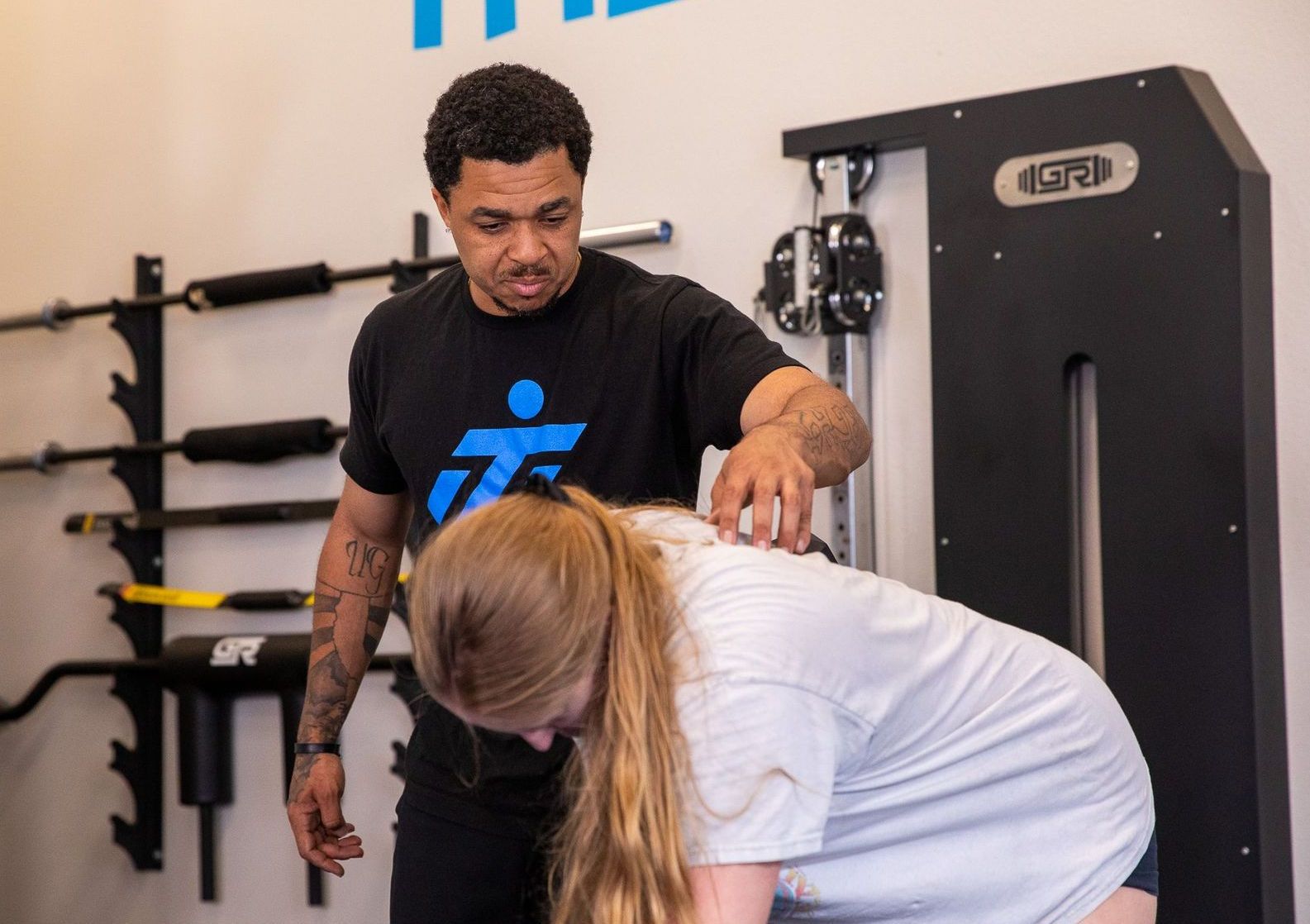 A man is helping a woman stretch her back in a gym.