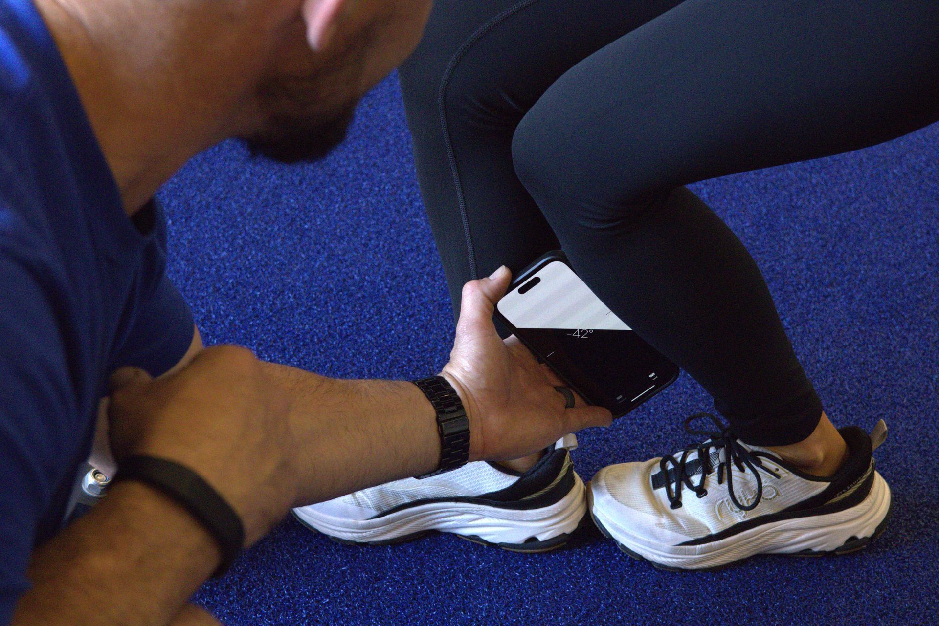 A man is stretching a woman 's leg in a gym.