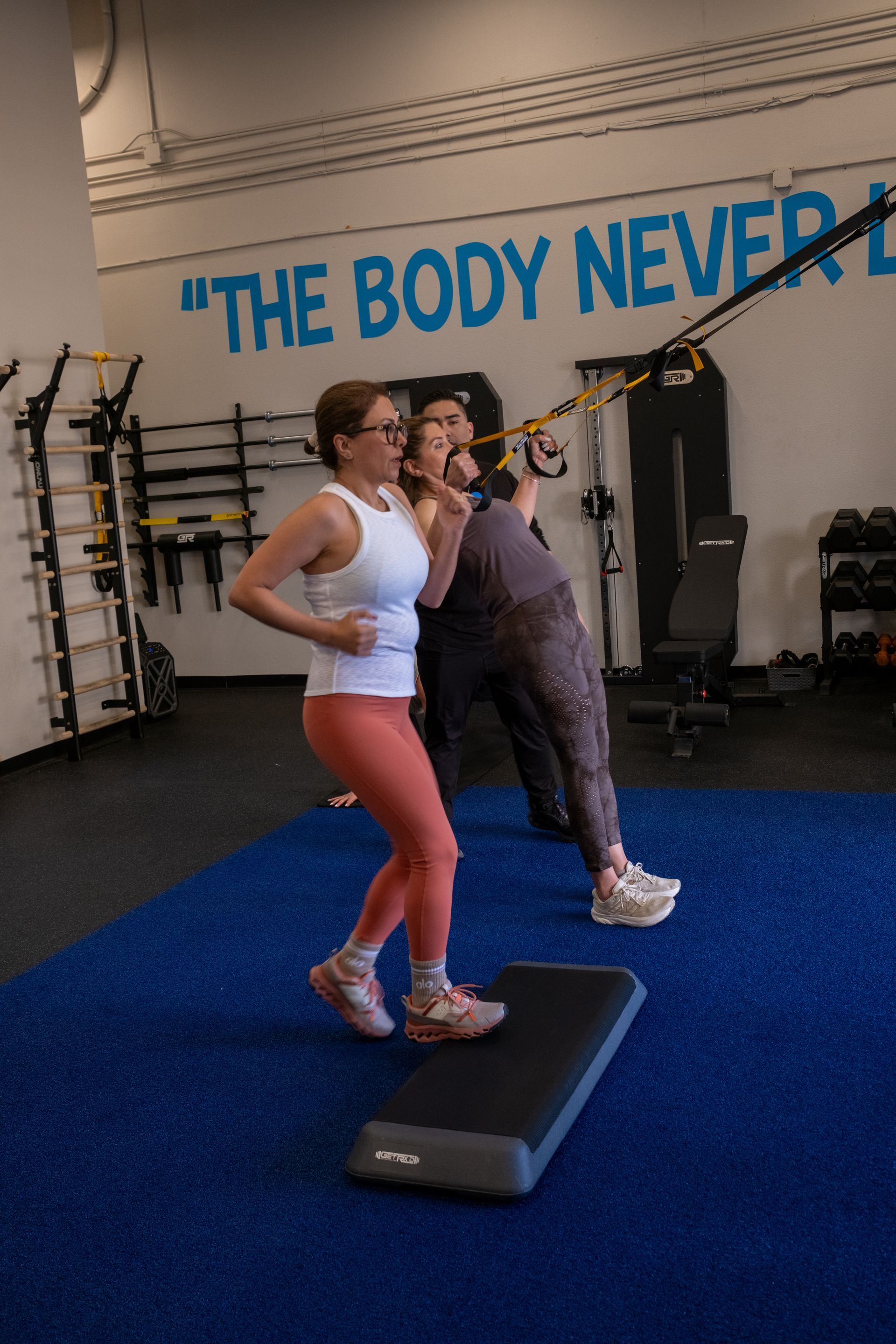 A man is helping a woman lift a barbell in a gym.