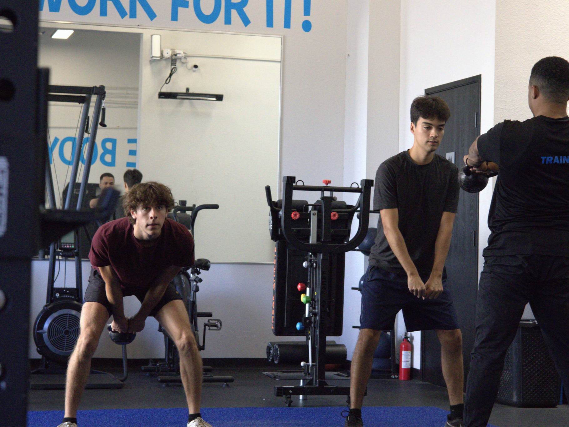 A man is helping a woman stretch her legs in a gym.