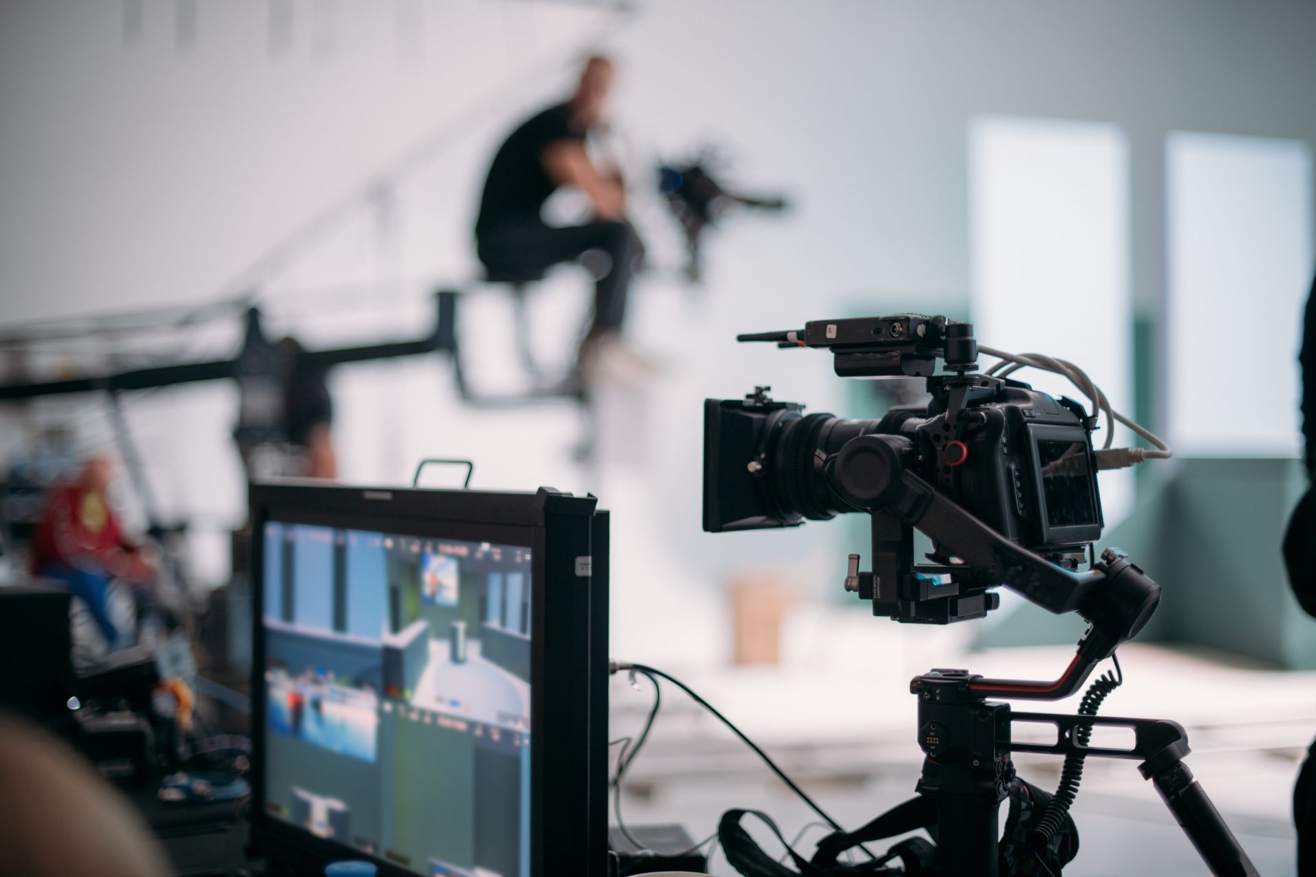 Camera on a tripod filming a scene; monitor shows footage. Studio setting.