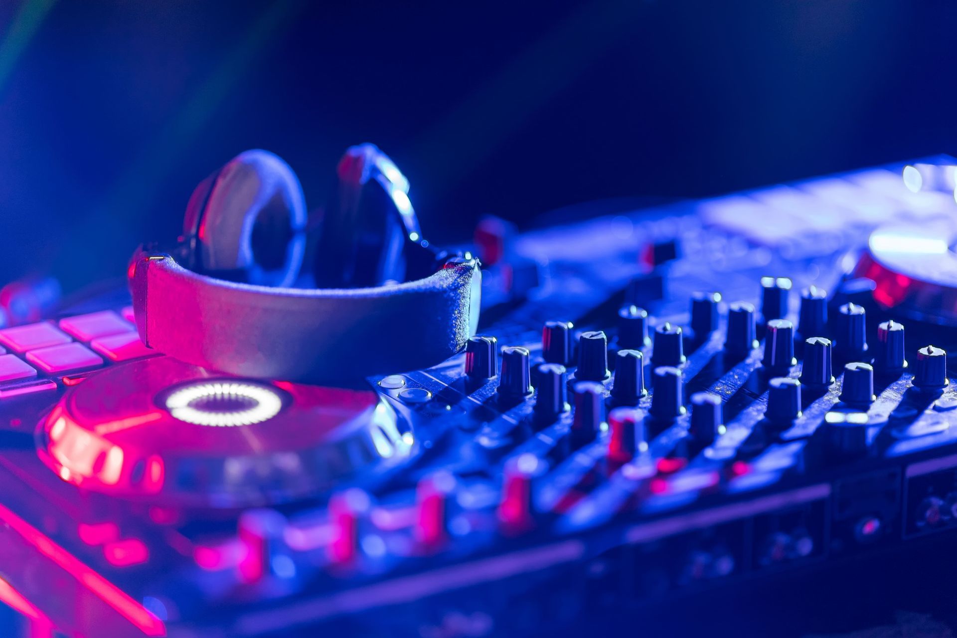 DJ mixer with headphones, lit by blue and pink lights.
