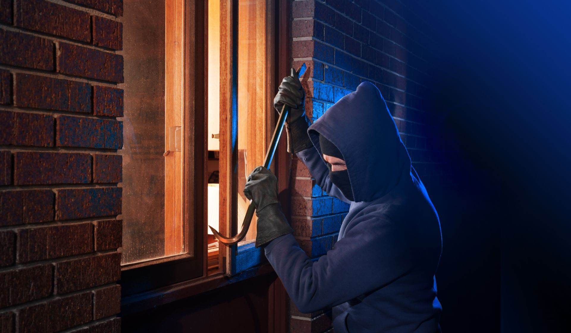 Man with hood breaking into a window