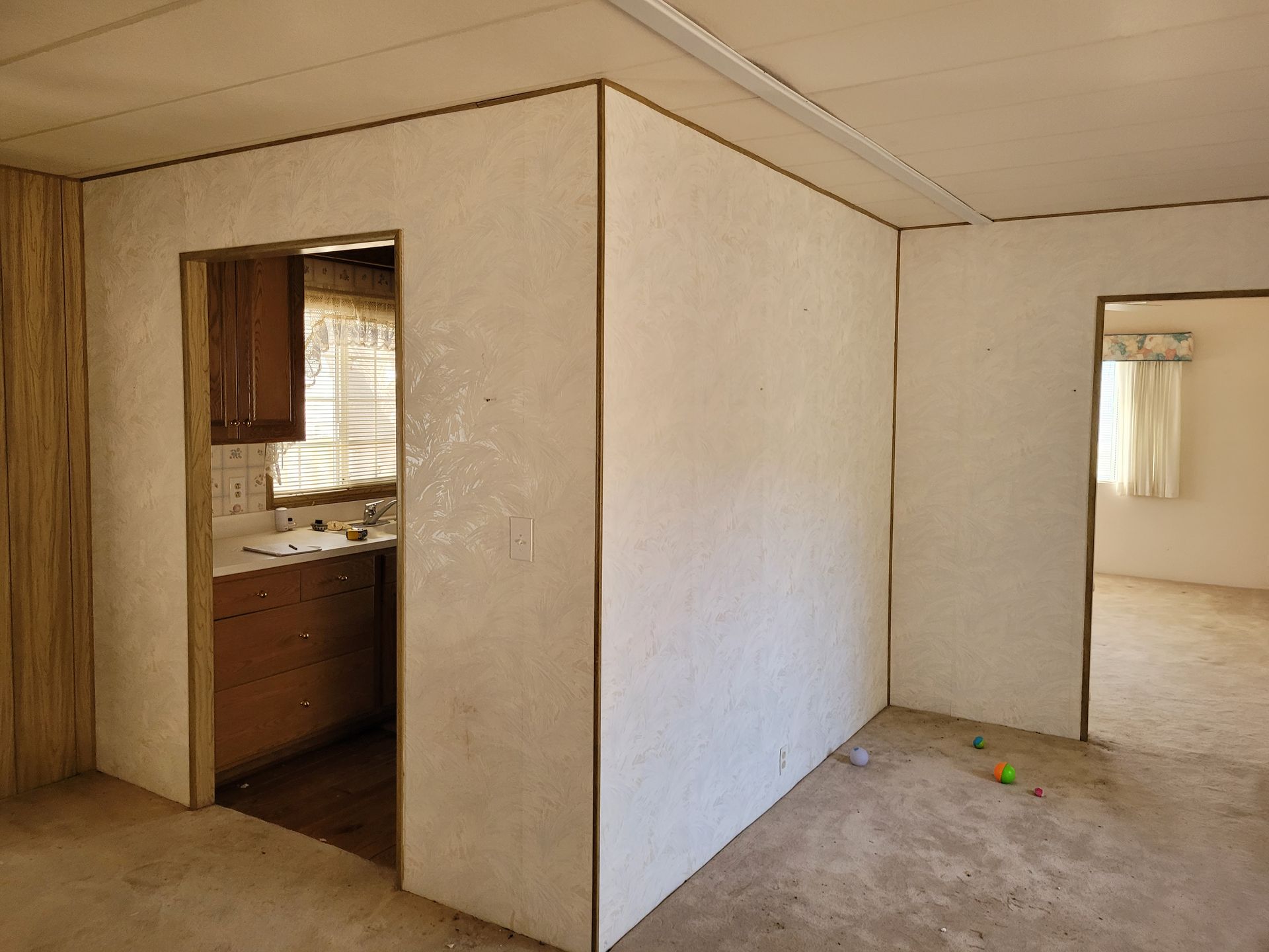 Interior of a room with textured white walls and doorways leading to the kitchen and another room. The floors are concrete.