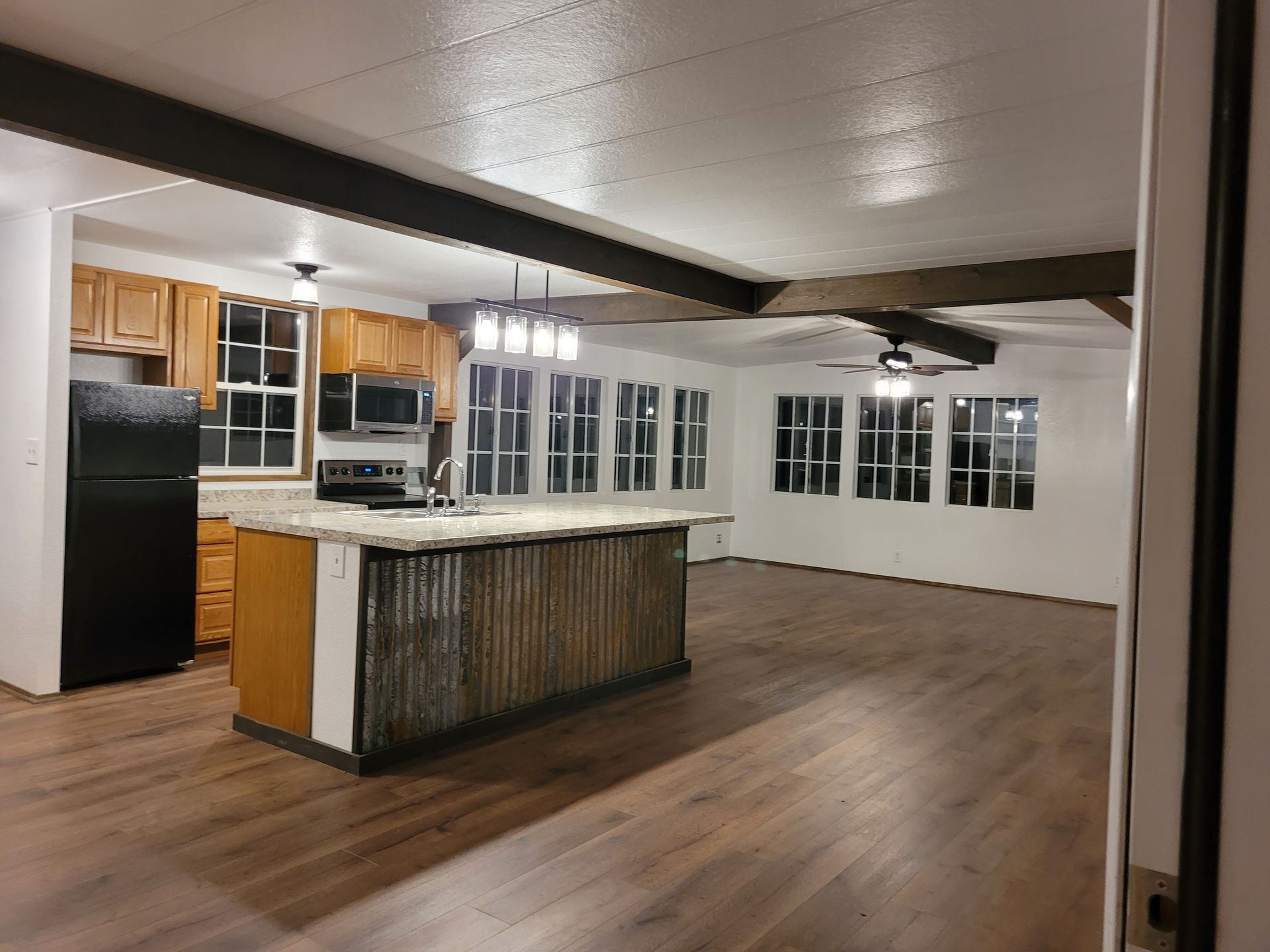 Spacious kitchen with wooden cabinets, black appliances, and a corrugated metal island. Hardwood floors and white walls.