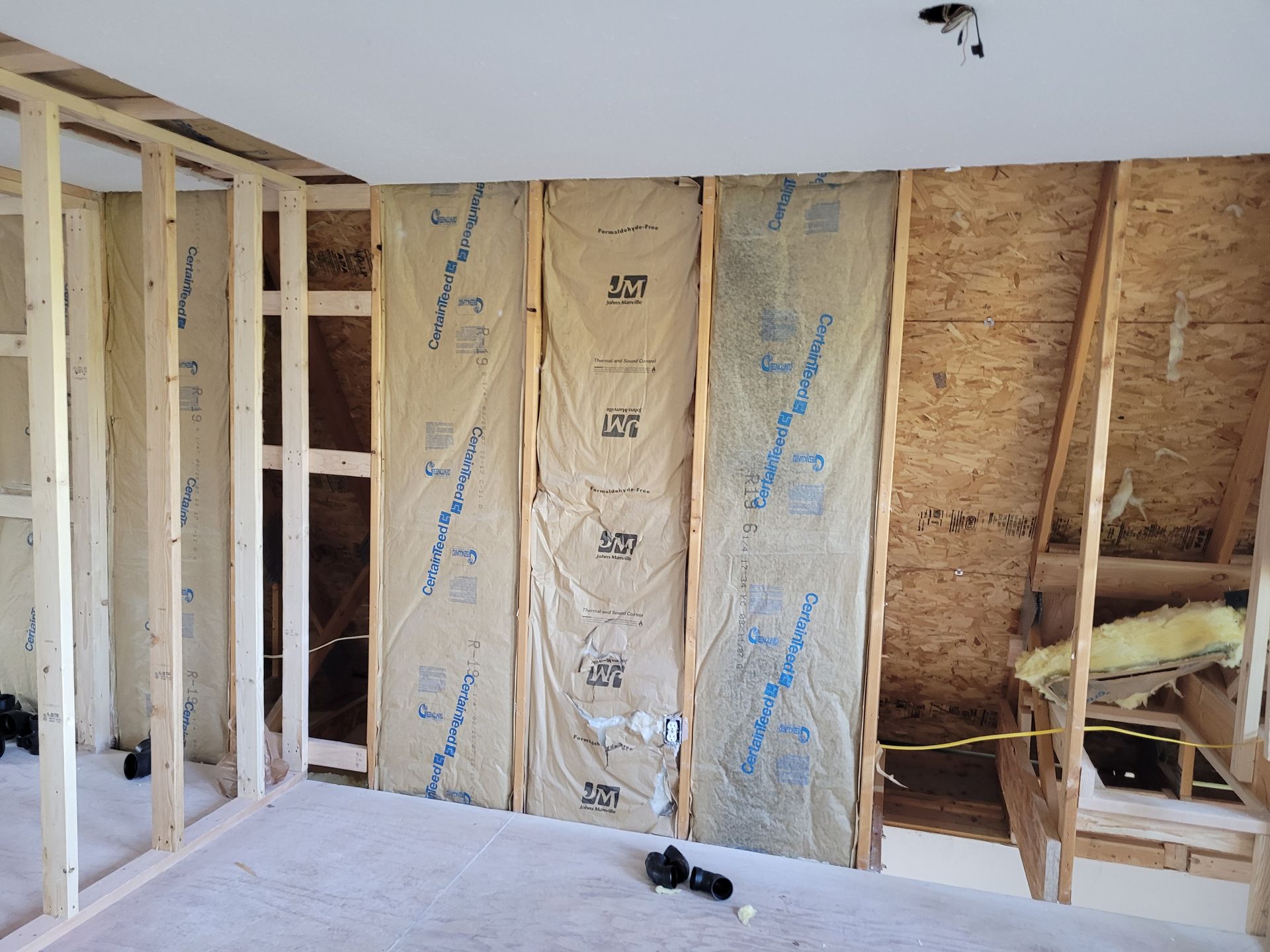 Interior framing of a room under construction, showing wooden studs, insulation, and a partial OSB wall.