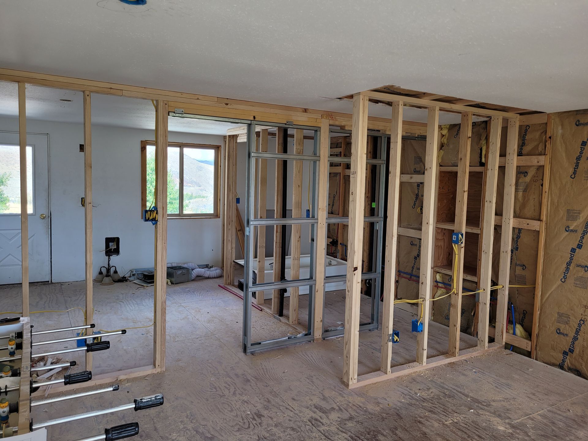 Interior of a room under construction, with wooden and metal stud framing for walls and doorways; exposed wiring.