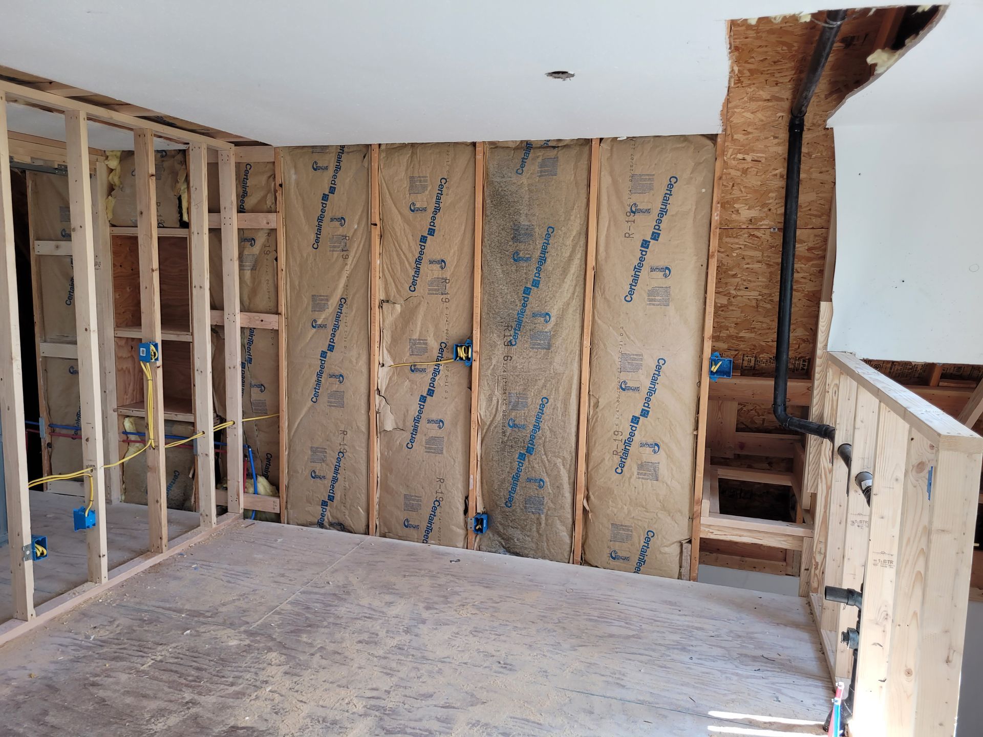 Interior construction: a room with exposed wooden wall studs and insulation. Electrical wiring and boxes are visible.