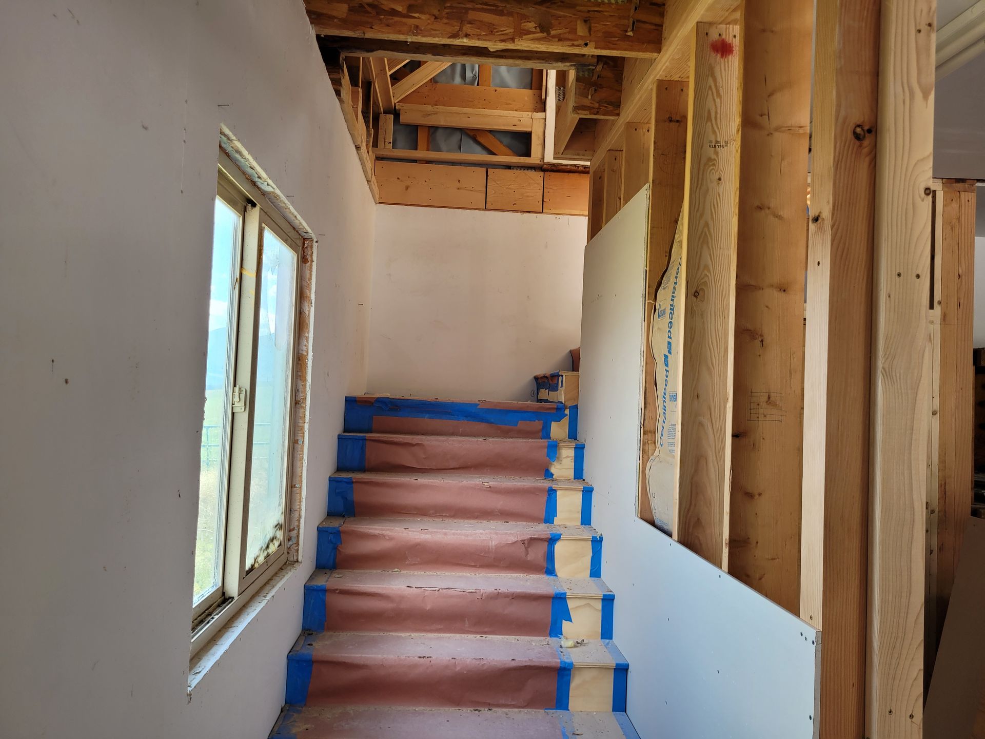 Staircase under construction with wood framing, drywall, and masking tape. A window is to the left.