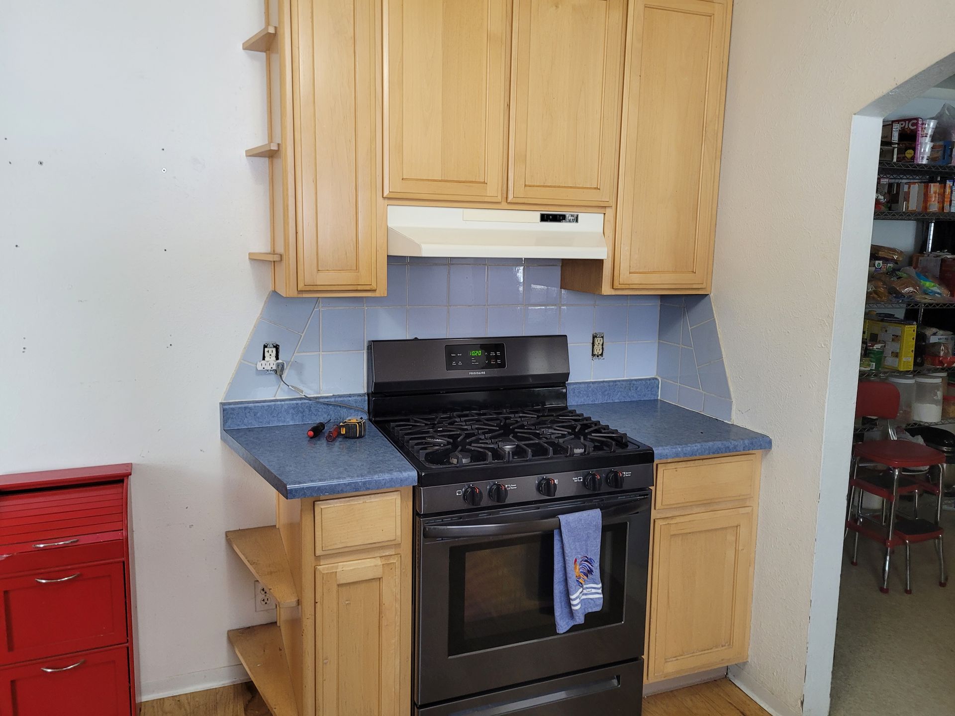 A kitchen with light-colored cabinets surrounding a black oven and stovetop. Blue countertops and a tiled backsplash are also visible.