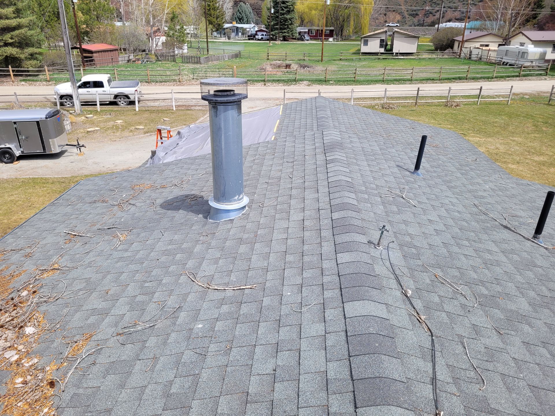 Overhead view of a grey shingle roof with a skylight, set in a residential area with houses and trees.