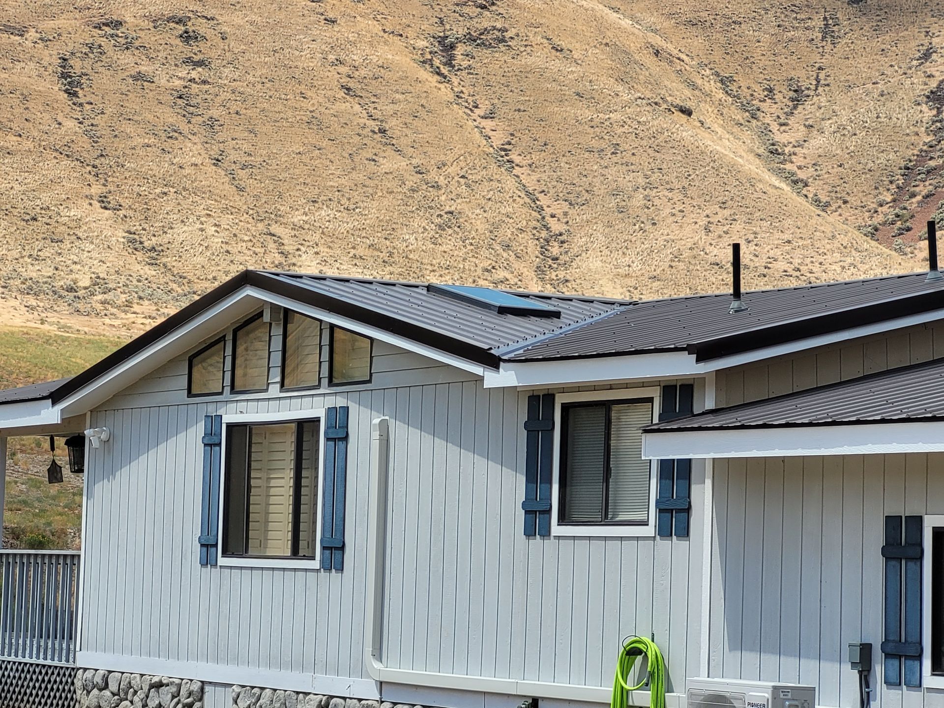 Light blue house with dark roof, blue shutters, and a mountain backdrop.