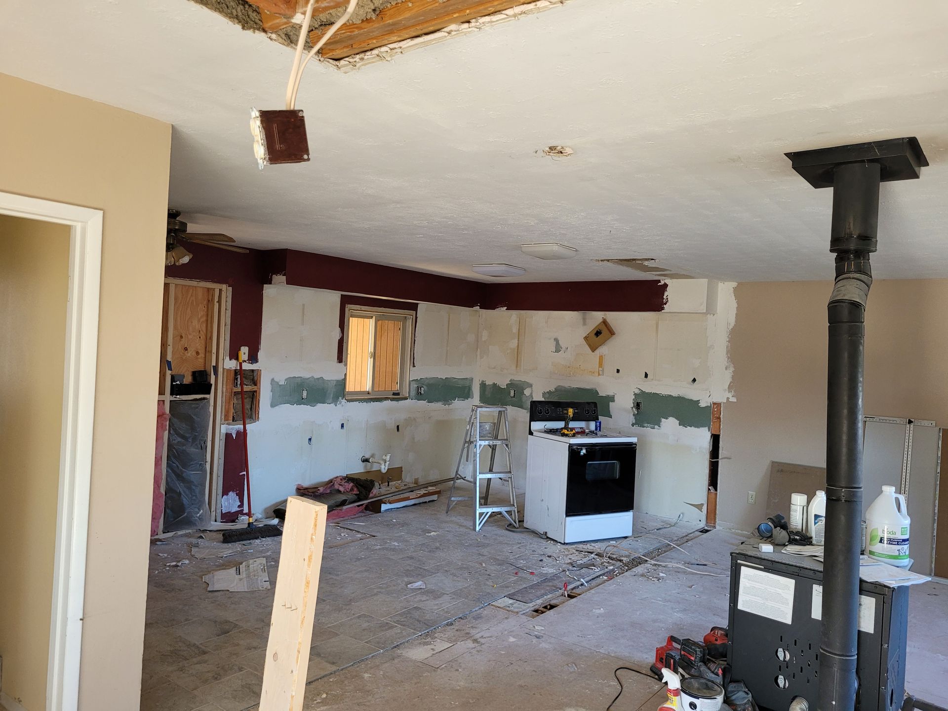 Kitchen during demolition, drywall removed from walls. Exposed wiring hangs from ceiling; wood and debris on floor.